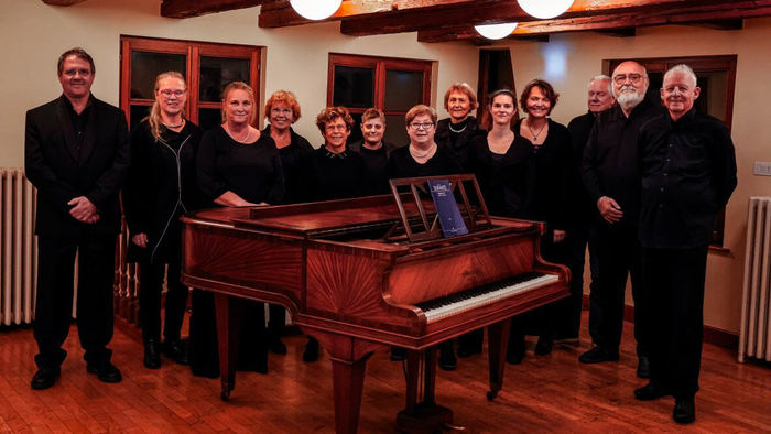 Un groupe de personnes posant autour d'un piano à queue dans une salle avec des poutres apparentes.
