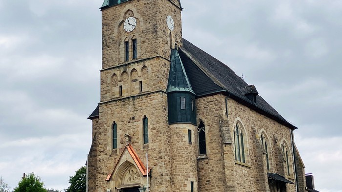 Historische Steinkirche mit Uhrturm und gewölbtem Eingang, vor bewölktem Himmel.