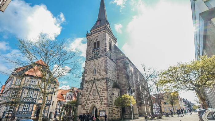 Historische Kirche mit hohem Turm in der Altstadt, Menschen gehen in der Nähe spazieren.