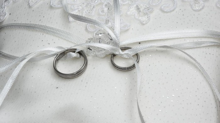 Zwei Ringe liegen auf weißem Stoff mit Spitzenborte und Schleifen.