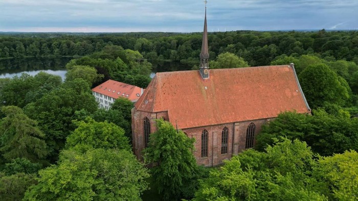 Kirchengebäude mit hohem Turm inmitten von Bäumen und Wasser.