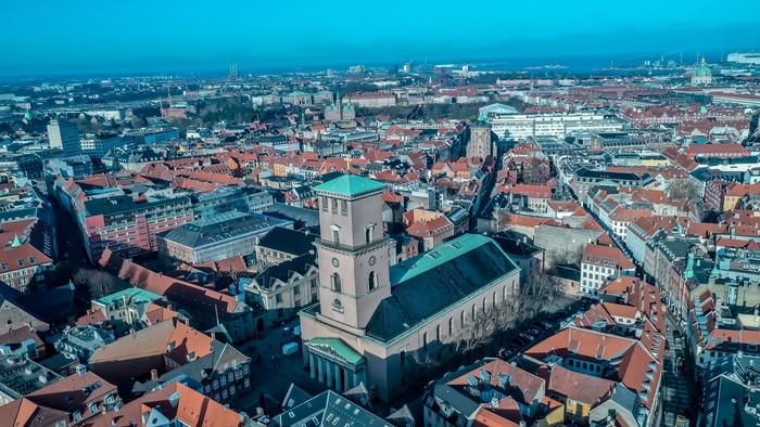 Luftfoto af en by med en markant kirke og bygninger med røde tage.