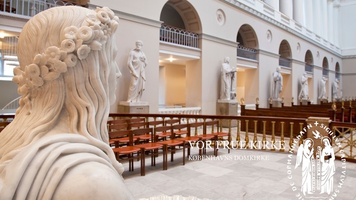 En kirkeinterior med marmorstatuer og træbænke.