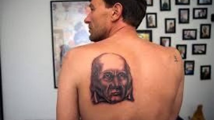 Mand med rykkert baghovedtattoo står i et rum med billeder på veggene