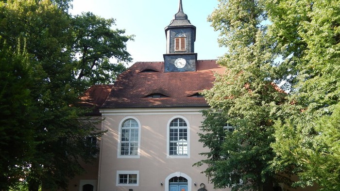 Das Bild zeigt eine Kirche mit Uhrturm und parkenden Autos davor.