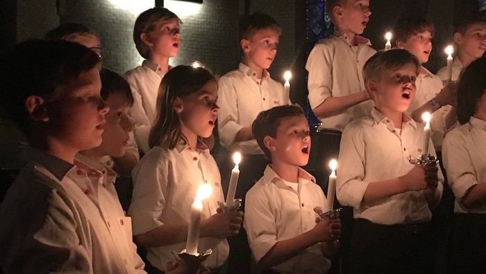 Børn synger og holder lys i mørke kirke.