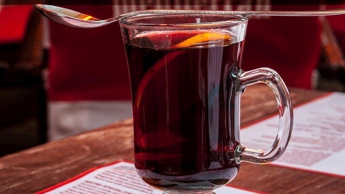 Glühweinbecher mit Zimt und Orange auf Tisch, Text in Deutsch