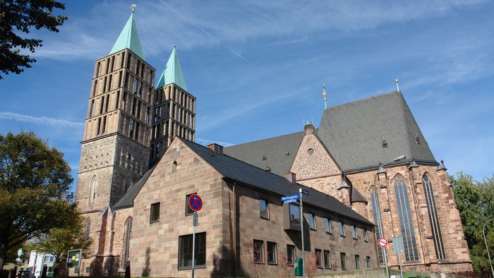 Große Kirche mit Zwillingstürmen und einem Kreuz obenauf, umgeben von Bäumen und Gebäuden.