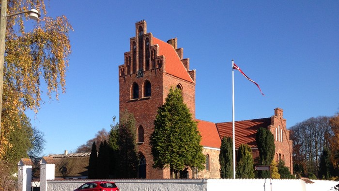 Røde kirke med tårn og bil i forgrunden