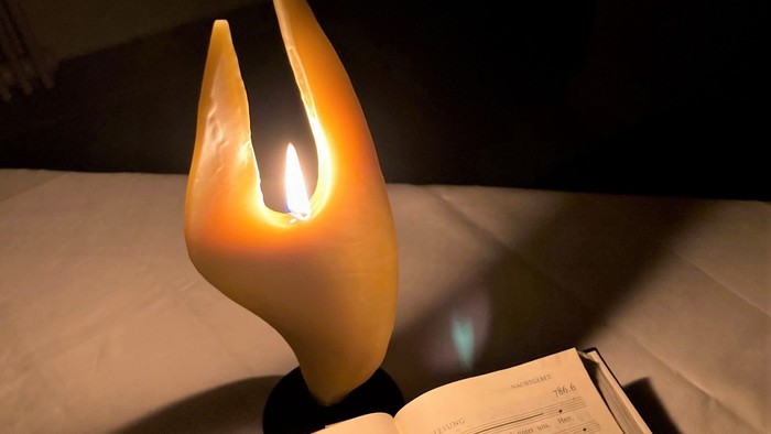 Ein beleuchteter Kerzenhalter steht auf einem Nachttisch neben einem aufgeschlagenen Buch.