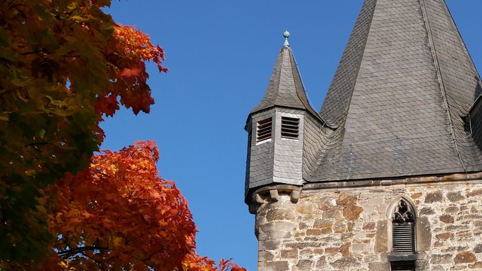 Steinschloss mit zwei Türmen und einem roten Dach, teilweise von Herbstblättern bedeckt.