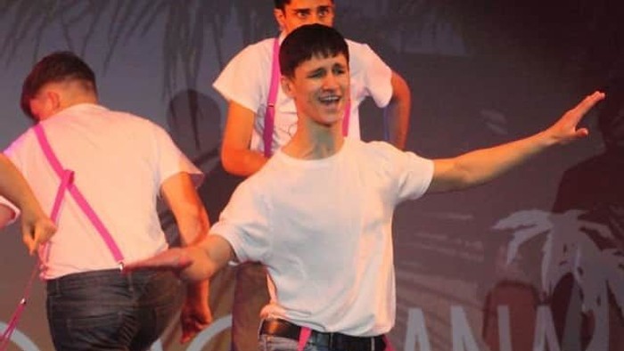 Three men dance on stage wearing suspenders