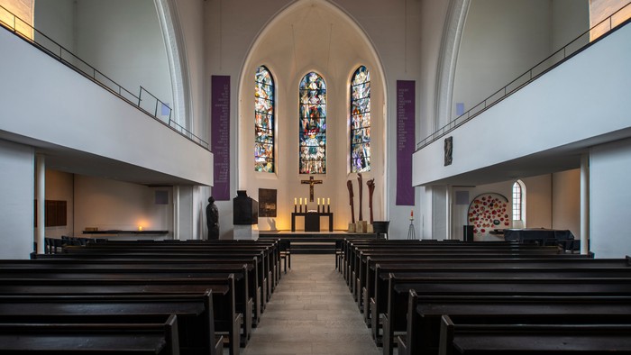 Leere Kirche mit Holzgebinden und buntem Fenster
