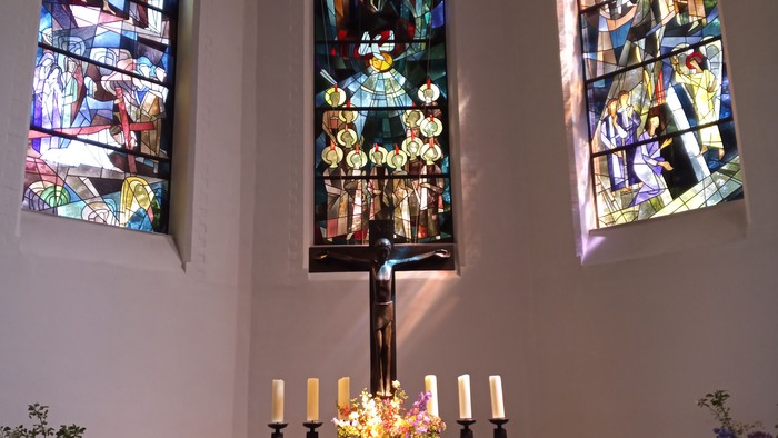 Farbenfrohe Kirchenfenster erleuchten den Altar mit Kerzen und Blumen.