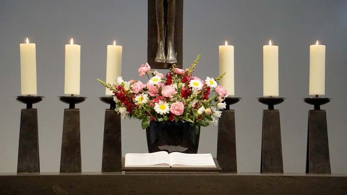 Ein Altar mit sechs brennenden Kerzen und einem Blumenstrauß