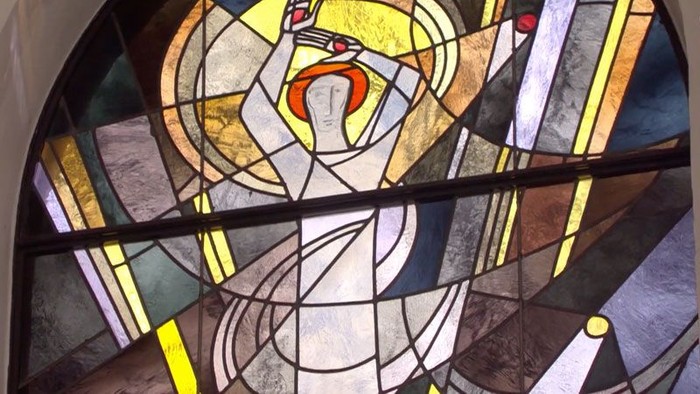 Das Bild zeigt ein buntes Kirchenfenster mit einem religiösen Motiv.