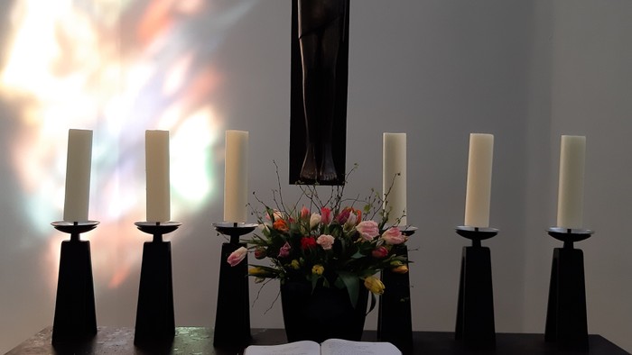 Kreuz, Kerzen, Blumen und Buch auf schwarzem Tisch