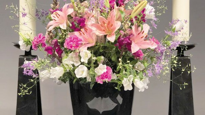 Blumengesteck und brennende Kerzen vor aufgeschlagenem Buch