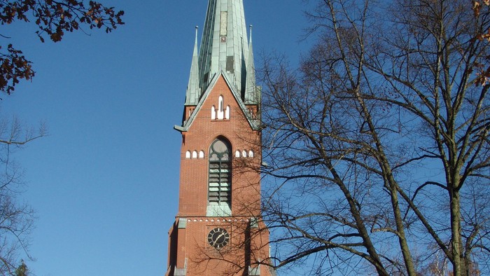 Große rote Kirche mit hohem Turm und grünem Dach in Parkanlage
