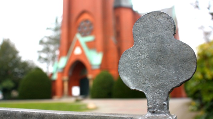 Eiserner Zaun vor rotem Kirchturm mit grünem Dach