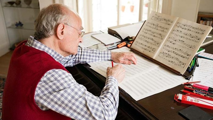 Ein älterer Mann liest Notenblätter an einem Schreibtisch.