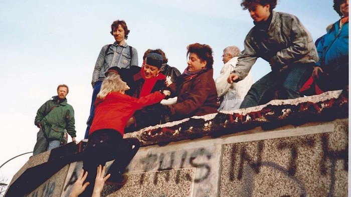 Menschen, die auf einer Betonkonstruktion sitzen und stehen, einige halten Babys.