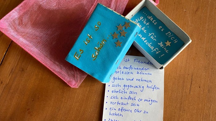 Ein pinkes Geschenkbeutel mit einer blauen Schachtel und einer weißen Karte darauf