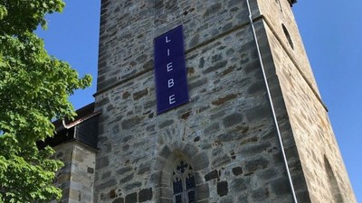 Steinerner Turm mit blauem Schild und Bank.