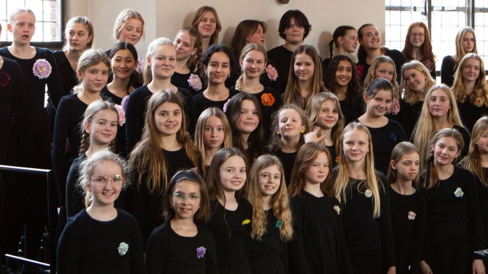 En stor kor, der består af både voksne og børn, poserer sammen i en kirke.