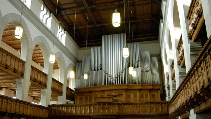 Große Kirche mit hölzernen Bänken und hohen Decken, beleuchtet von mehreren Kronleuchtern
