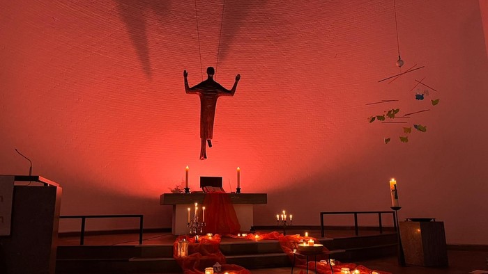 Eine Kirche mit einer Figur und vielen Kerzen im roten Licht.