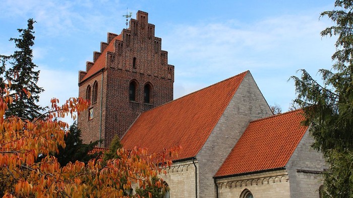Gammel kirke med tegltag og højt tårn i forgrunden