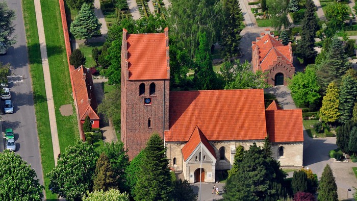 En kirke med røde tag og omgivelser med træer og græsplæne