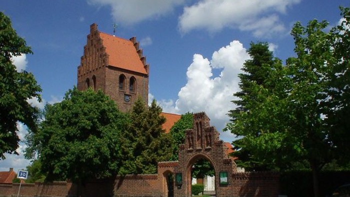 En rød murstenskirke med tårn og ark i en park.