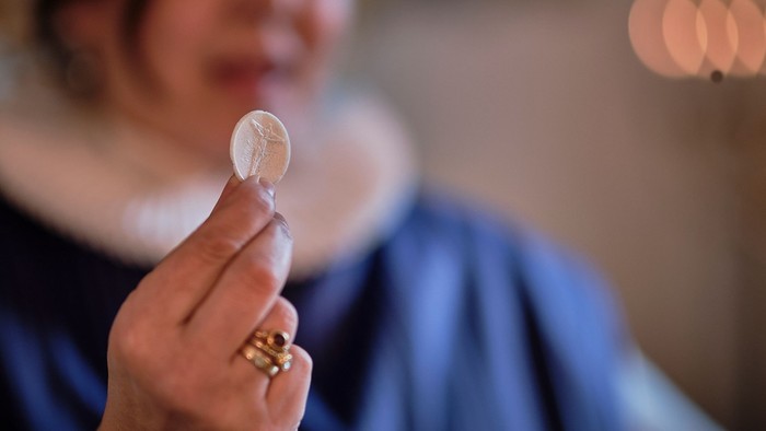 En person holder en mynt op foran ansigtet.