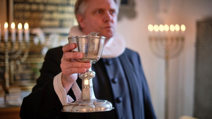 Mand i mørkt tøj holder en sølv kalk i kirke