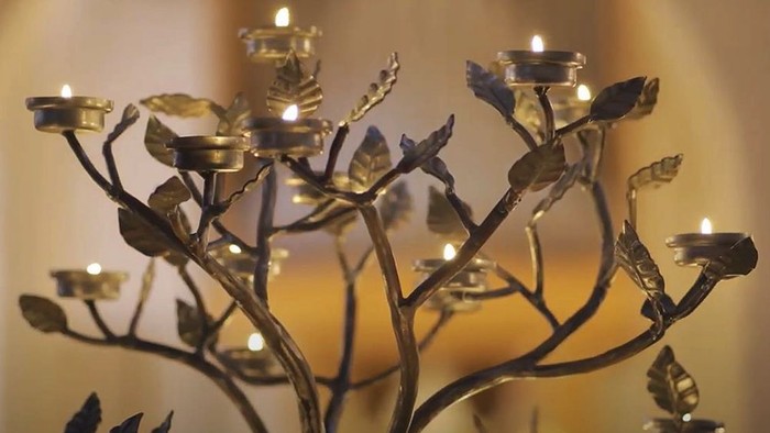 En smuk brændestage med blomster og blader, belyst af lyse lys.