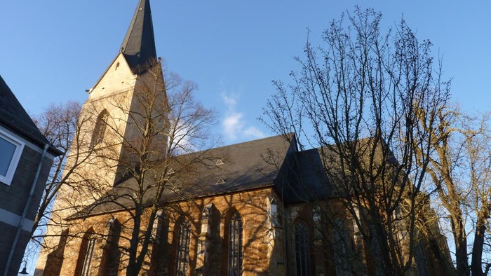 Kirche mit hohem Kirchturm und Rundbogenfenstern, umgeben von Bäumen.