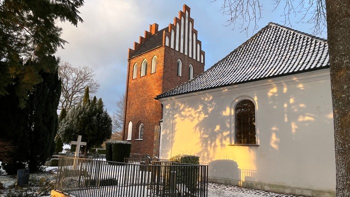 En snedækket kirkegård med en rød murstenskirke og et hvidt sidebygning.
