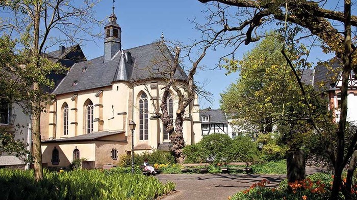 Ein altes Gebäude mit einem Turm, umgeben von Bäumen und einem Garten