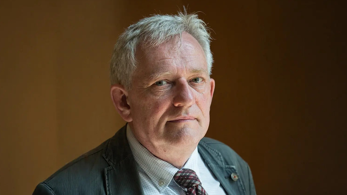En middelalderlig mand med kort hår og skæg, der bærer en mørk suite og rød halsbånd.