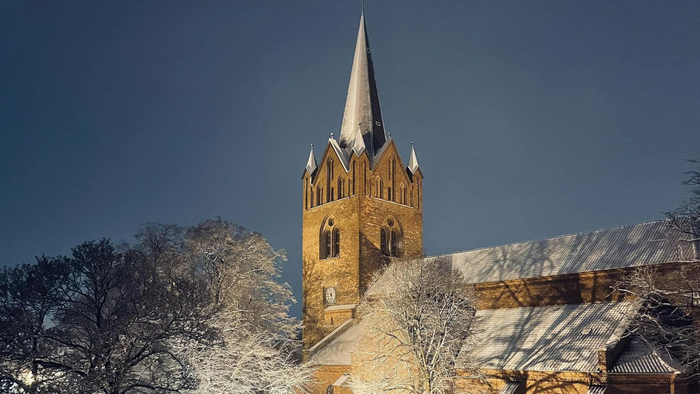 En belyset kirke med tårn i snødekt bymiljø.