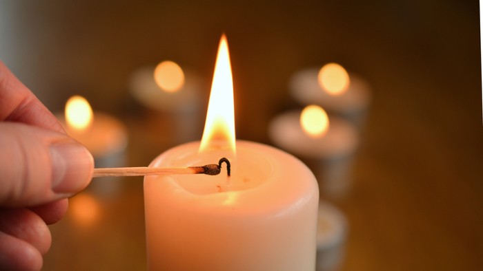 En hånd tænder en lyse stearinlys med en tændstik
