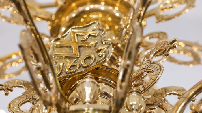 Forviklet gyldenfarvet krystallysekrone med detaljerede mønstre og flere etager.