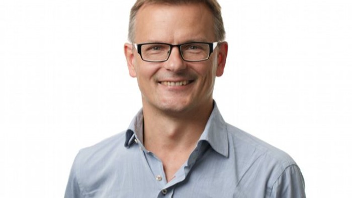 En smilende mand med briller og blå skjorte.