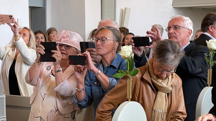 En gruppe mennesker i kirke, nogle tager billeder med mobiltelefoner