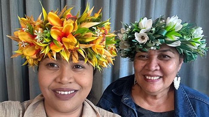 Zwei Frauen mit Blumenkränzen lächeln in die Kamera.