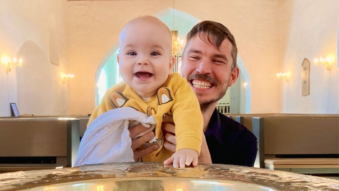 En mand holder et spæd barn i en kirke ved et font.