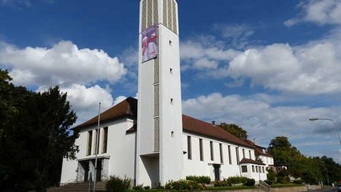 Moderne Kirche mit hohem Glockenturm vor einem strahlend blauen Himmel mit vereinzelten Wolken.
