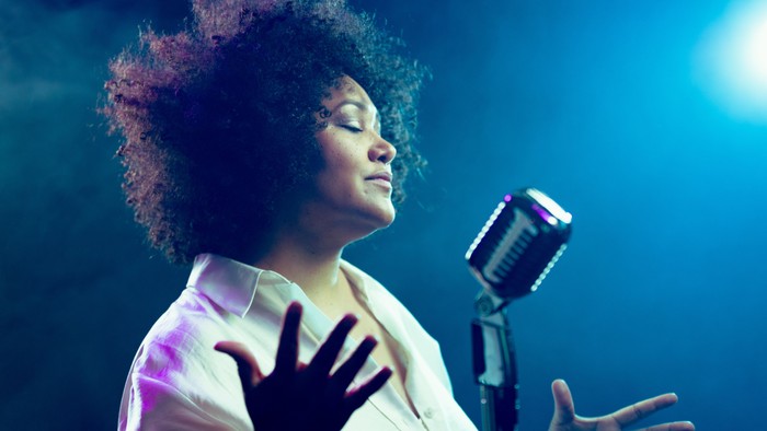 Eine Frau singt leidenschaftlich in ein Mikrofon auf der Bühne.